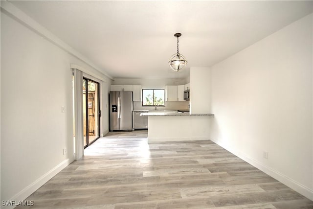 interior space featuring stainless steel appliances, light wood-type flooring, a peninsula, and white cabinetry