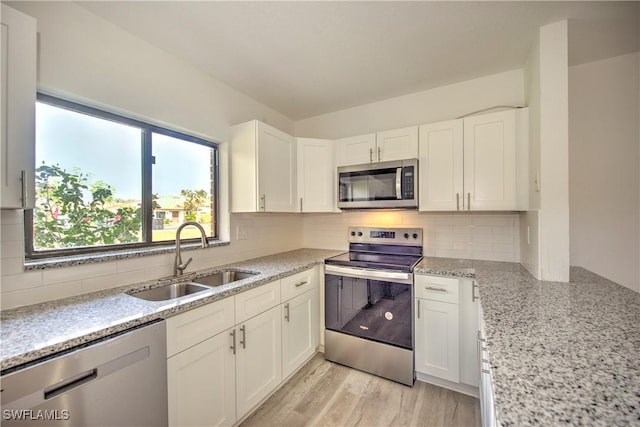 kitchen with a sink, white cabinetry, light wood-style floors, appliances with stainless steel finishes, and backsplash