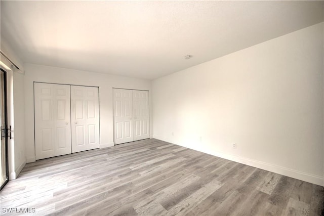 unfurnished bedroom featuring light wood-type flooring, baseboards, and two closets