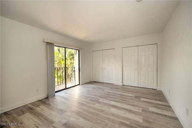 unfurnished bedroom featuring access to outside, baseboards, light wood finished floors, and two closets