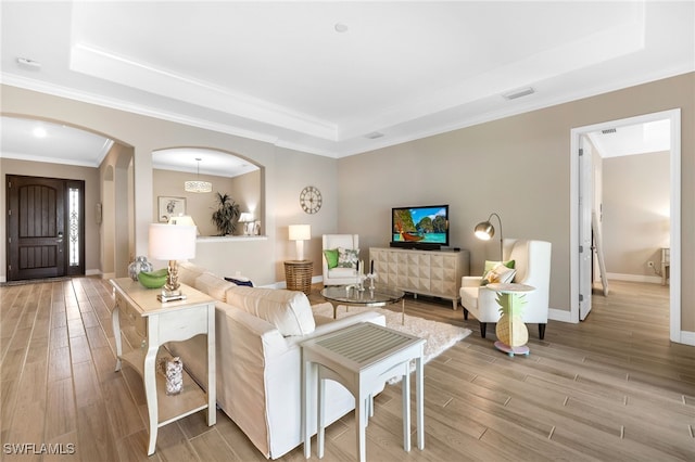 living room with arched walkways, light wood-style flooring, visible vents, baseboards, and a tray ceiling