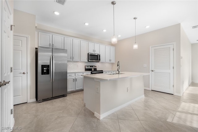 kitchen featuring a kitchen island with sink, stainless steel appliances, a sink, hanging light fixtures, and tasteful backsplash