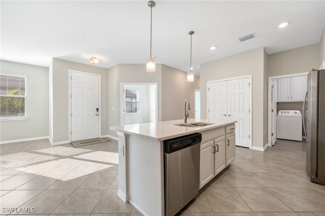 kitchen featuring appliances with stainless steel finishes, washer / clothes dryer, a kitchen island with sink, light countertops, and a sink