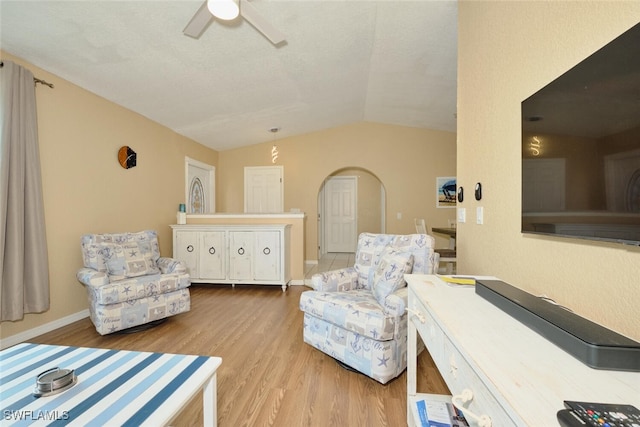 living area featuring arched walkways, lofted ceiling, light wood-style floors, ceiling fan, and baseboards