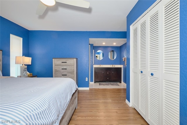 bedroom featuring ensuite bathroom, ceiling fan, baseboards, a closet, and light wood finished floors