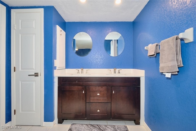 bathroom featuring a textured wall, a sink, baseboards, and double vanity