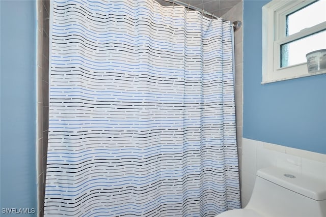 bathroom featuring tiled shower, wainscoting, toilet, and tile walls