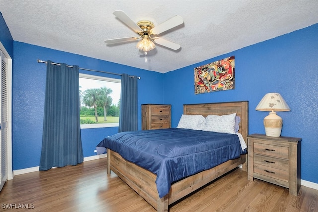 bedroom with a textured ceiling, ceiling fan, a textured wall, wood finished floors, and baseboards