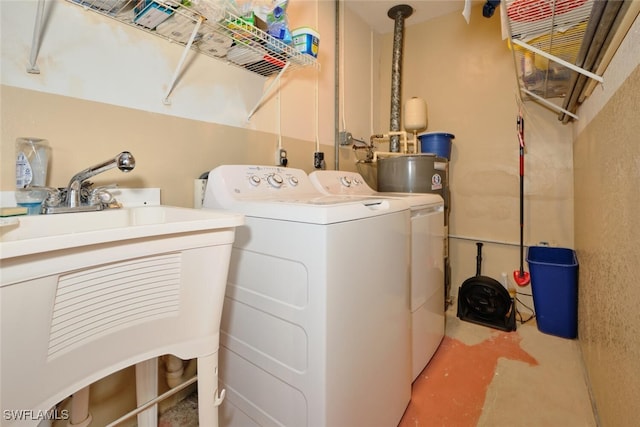 clothes washing area featuring water heater, laundry area, separate washer and dryer, and a sink