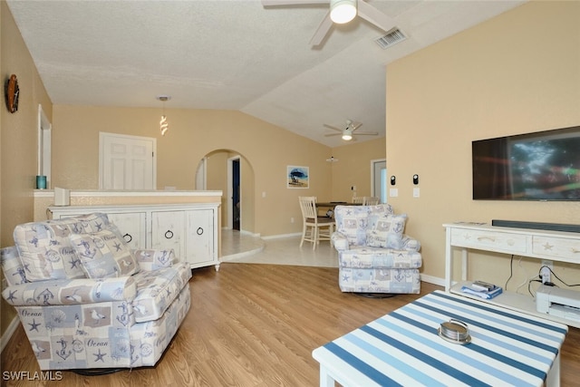 living room with arched walkways, lofted ceiling, visible vents, light wood-style floors, and ceiling fan