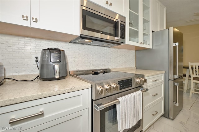 kitchen with decorative backsplash, glass insert cabinets, appliances with stainless steel finishes, marble finish floor, and light countertops