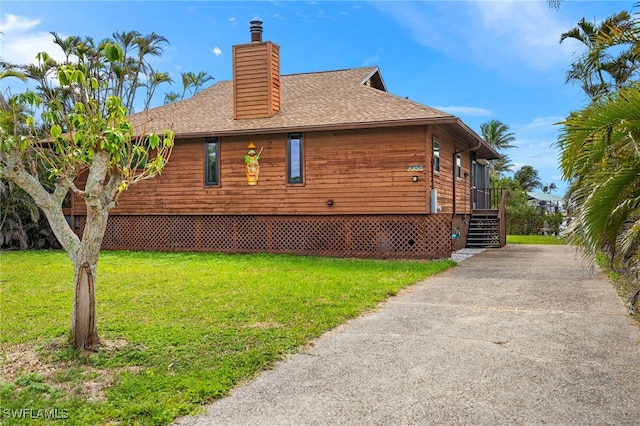 view of side of home with a shingled roof, a lawn, and a chimney