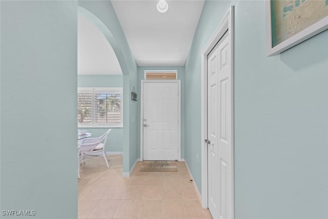 foyer featuring arched walkways, light tile patterned floors, and baseboards