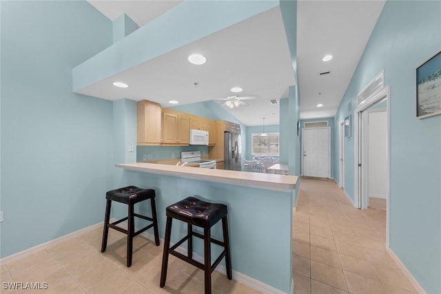 kitchen featuring white appliances, a breakfast bar, a peninsula, light countertops, and light brown cabinets