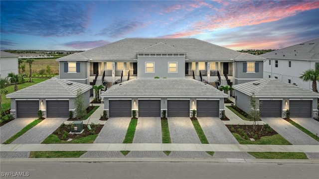 multi unit property with driveway, a garage, a tile roof, stairway, and stucco siding