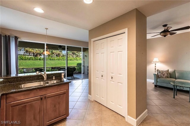 kitchen featuring light tile patterned floors, a sink, hanging light fixtures, brown cabinetry, and dark stone countertops