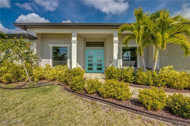 entrance to property featuring stucco siding, covered porch, a lawn, and french doors