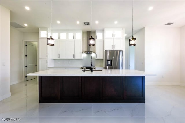 kitchen with a large island, visible vents, glass insert cabinets, wall chimney range hood, and stainless steel fridge