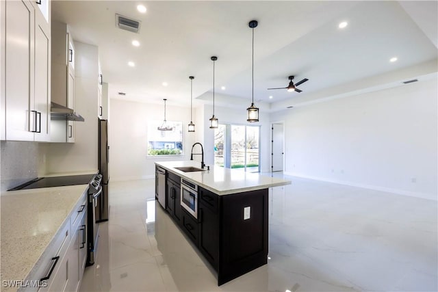 kitchen featuring stainless steel appliances, a sink, white cabinets, a center island with sink, and decorative light fixtures