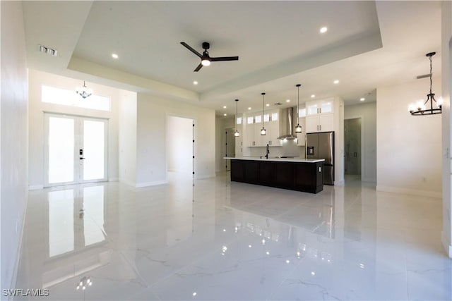 unfurnished living room with visible vents, a raised ceiling, ceiling fan with notable chandelier, french doors, and recessed lighting