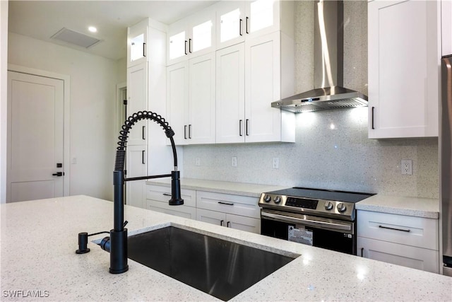 kitchen featuring glass insert cabinets, stainless steel range with electric cooktop, a sink, wall chimney range hood, and white cabinetry