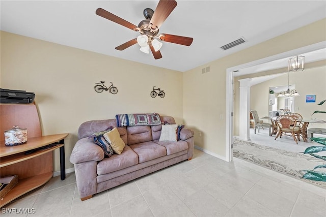 living room featuring ceiling fan with notable chandelier, visible vents, baseboards, and light tile patterned flooring