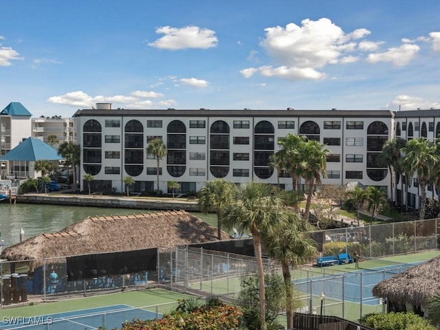 view of tennis court featuring a water view and fence