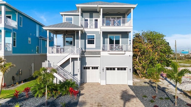 raised beach house with decorative driveway, a standing seam roof, metal roof, a garage, and stairs