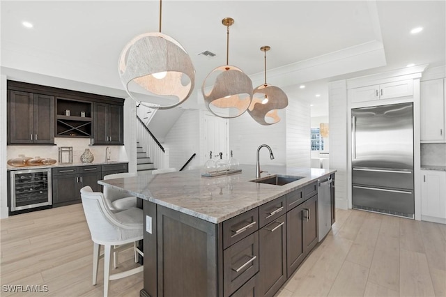 kitchen with beverage cooler, appliances with stainless steel finishes, dark brown cabinets, open shelves, and a sink