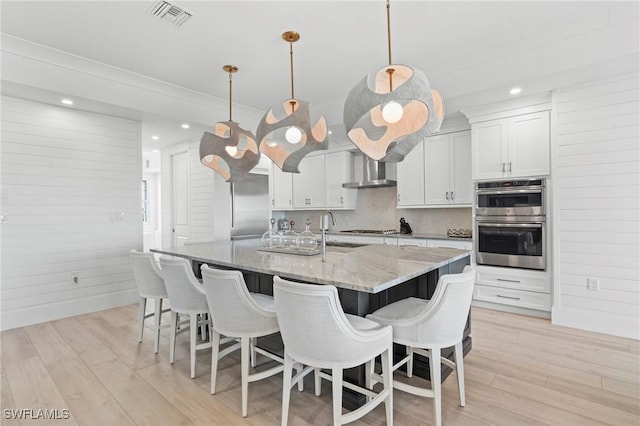 kitchen with double oven, visible vents, light wood-style flooring, and wall chimney exhaust hood