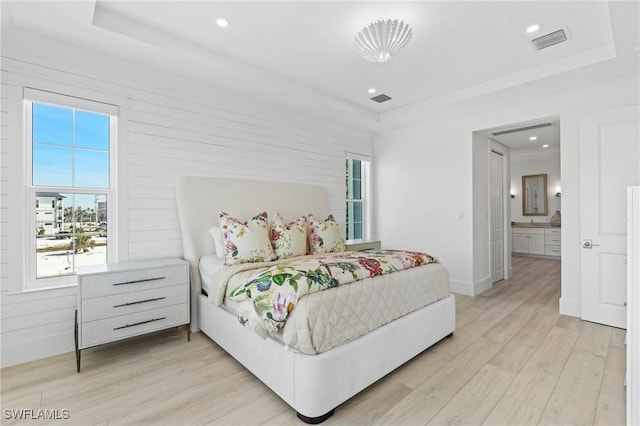 bedroom with a tray ceiling, visible vents, and light wood-style flooring