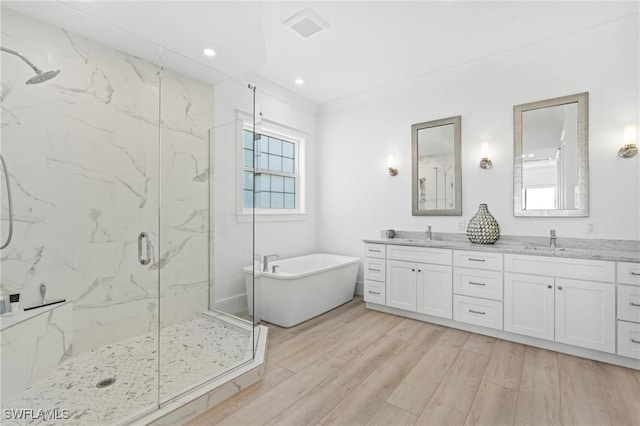 full bathroom featuring a freestanding bath, a marble finish shower, a sink, and wood finished floors