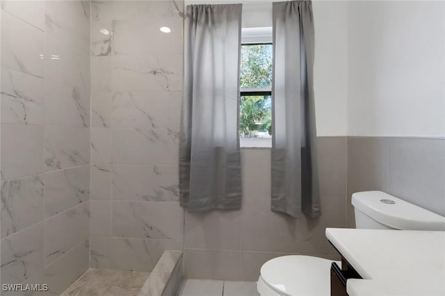 bathroom featuring toilet, a tile shower, tile walls, and vanity