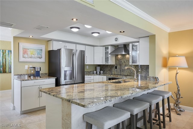 kitchen with wall chimney exhaust hood, white cabinetry, stainless steel refrigerator with ice dispenser, and light stone counters