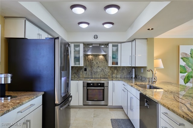 kitchen featuring a sink, white cabinetry, appliances with stainless steel finishes, wall chimney exhaust hood, and glass insert cabinets