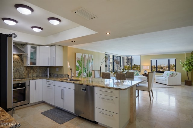 kitchen featuring white cabinets, glass insert cabinets, a peninsula, light stone countertops, and stainless steel appliances