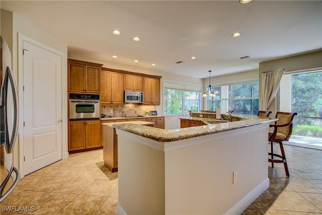 kitchen featuring brown cabinetry, decorative backsplash, a large island, stainless steel appliances, and a sink