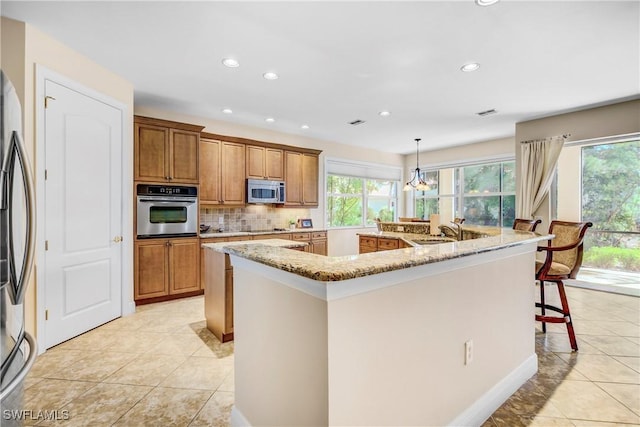 kitchen with stainless steel appliances, a spacious island, a sink, brown cabinets, and decorative backsplash