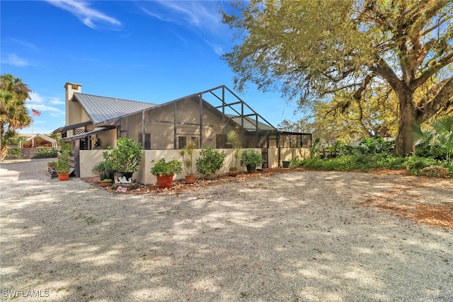 view of side of property with a standing seam roof, metal roof, a chimney, and a lanai