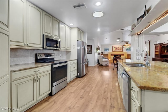 kitchen with visible vents, appliances with stainless steel finishes, open floor plan, light stone countertops, and a sink