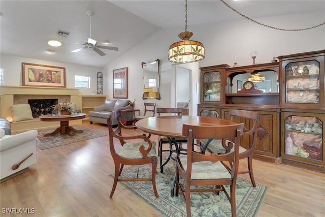 dining space featuring vaulted ceiling, visible vents, a fireplace, and light wood finished floors