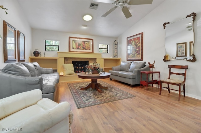 living room featuring a fireplace, lofted ceiling, visible vents, light wood-style floors, and ceiling fan