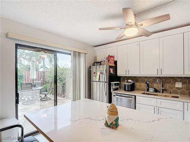 kitchen with stainless steel appliances, tasteful backsplash, a sink, and white cabinetry