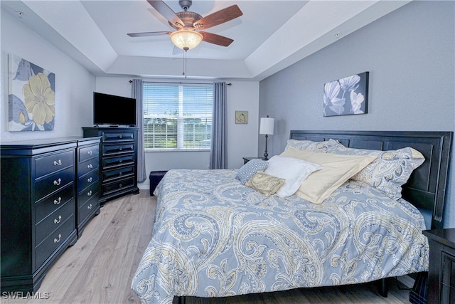 bedroom featuring light wood finished floors, a tray ceiling, and a ceiling fan