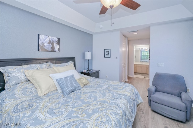 bedroom featuring light wood finished floors, ensuite bath, visible vents, and ceiling fan