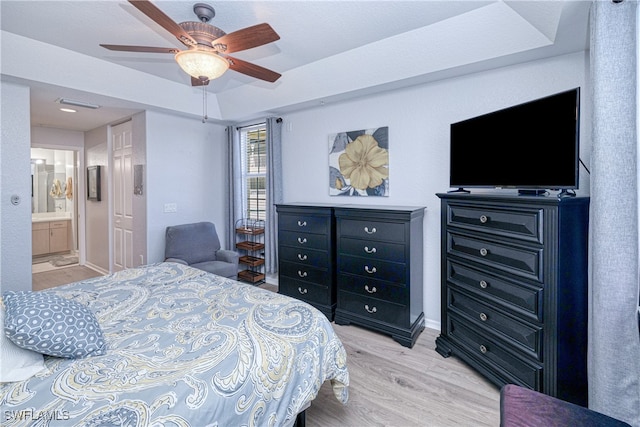 bedroom with light wood-style flooring, a tray ceiling, ceiling fan, and connected bathroom