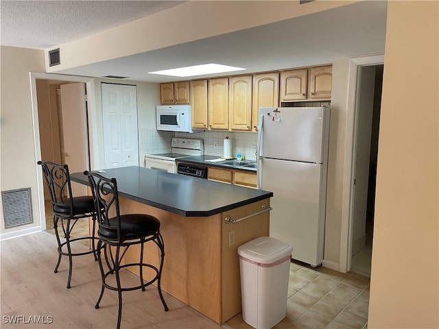 kitchen featuring white appliances, dark countertops, visible vents, and a center island