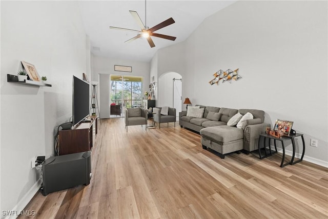 living room featuring arched walkways, high vaulted ceiling, a ceiling fan, baseboards, and light wood finished floors