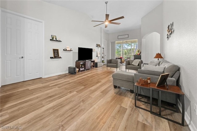 living area featuring arched walkways, light wood-style flooring, a high ceiling, ceiling fan, and baseboards