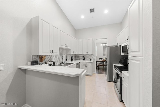 kitchen with a peninsula, a sink, white cabinetry, appliances with stainless steel finishes, and backsplash